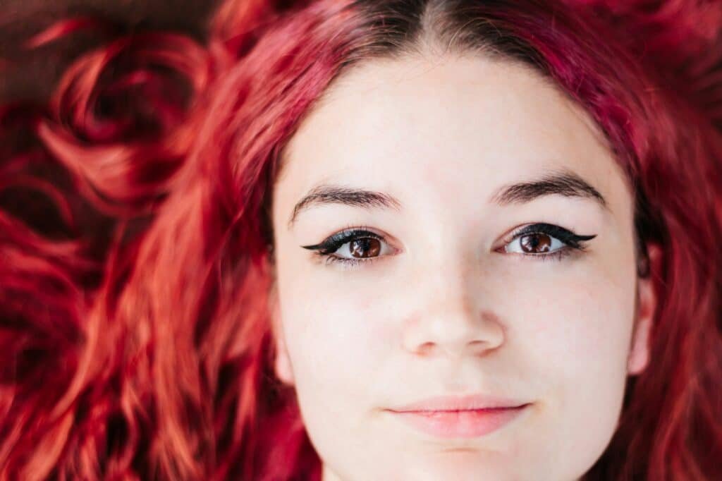 red wig Top portrait of young and teenage woman with white skin and red, shiny, wavy hair.