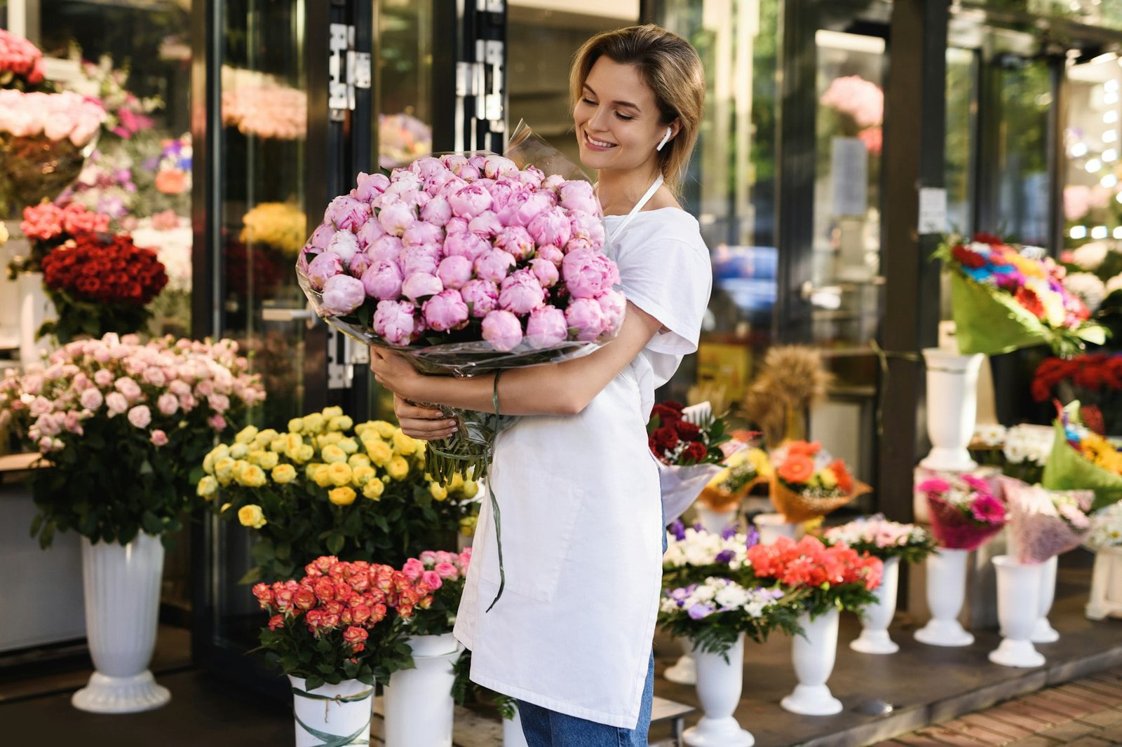 Just Flowers Woman florist with a heap of pink peony flowers in her little flower shop